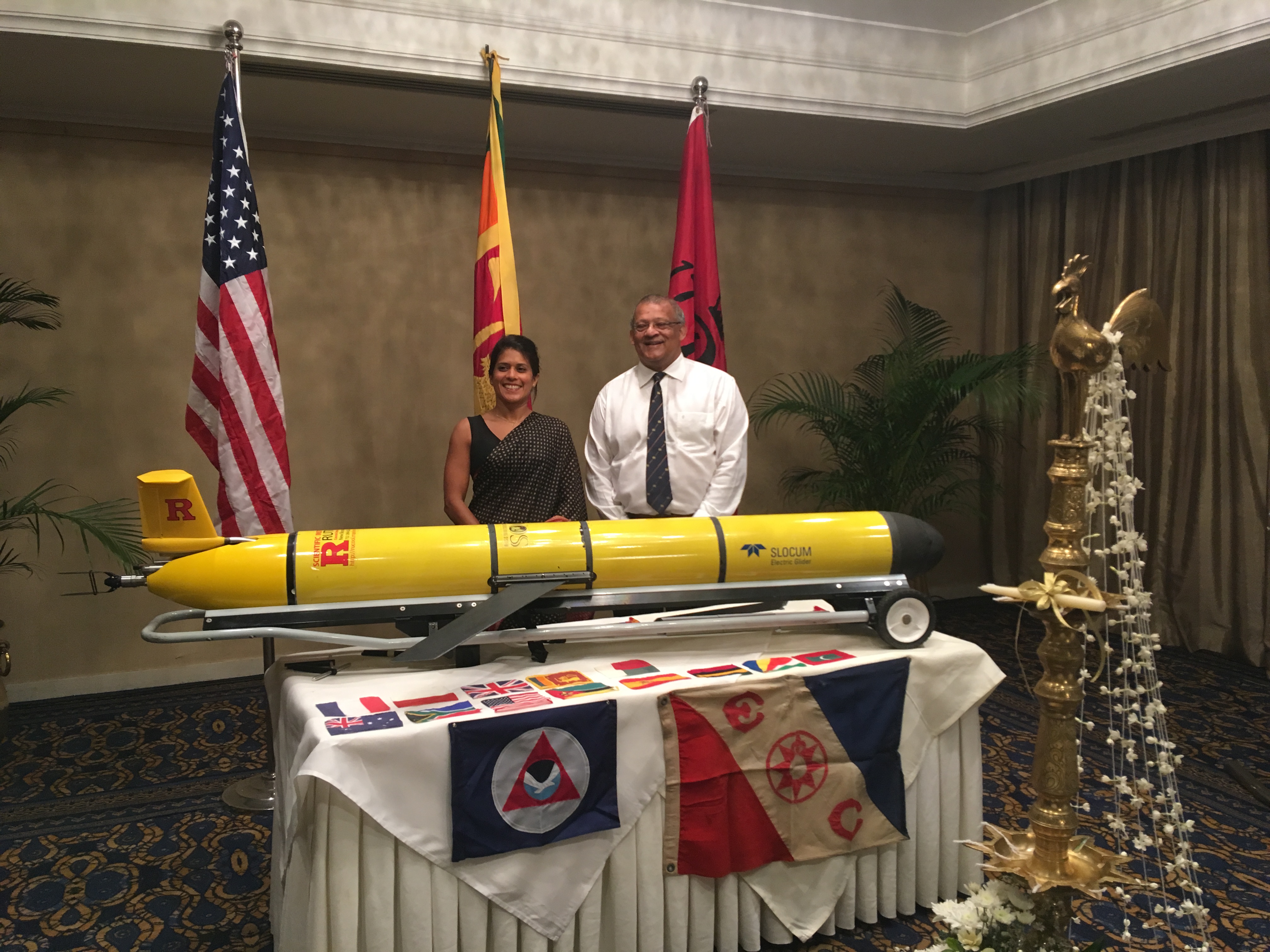 RU29 is prepared for a welcoming ceremony in Colombo, Sri Lanka organized by Prof. Chari Pattiaratchi (right). Dr. Asha de Vos (left) served as Master of Ceremonies. Displayed flags include U.S., Sri Lanka and Rutgers (on stands), NOAA and Explorers Club (side of table), and the international partners (tabletop). A traditional Sri Lanka oil lamp was lighted to open the ceremony.